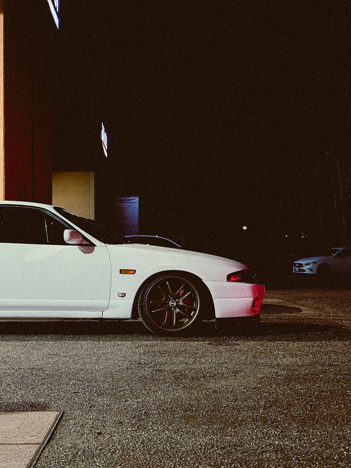 White sports car parked at night, showcasing sleek design and modern wheels.